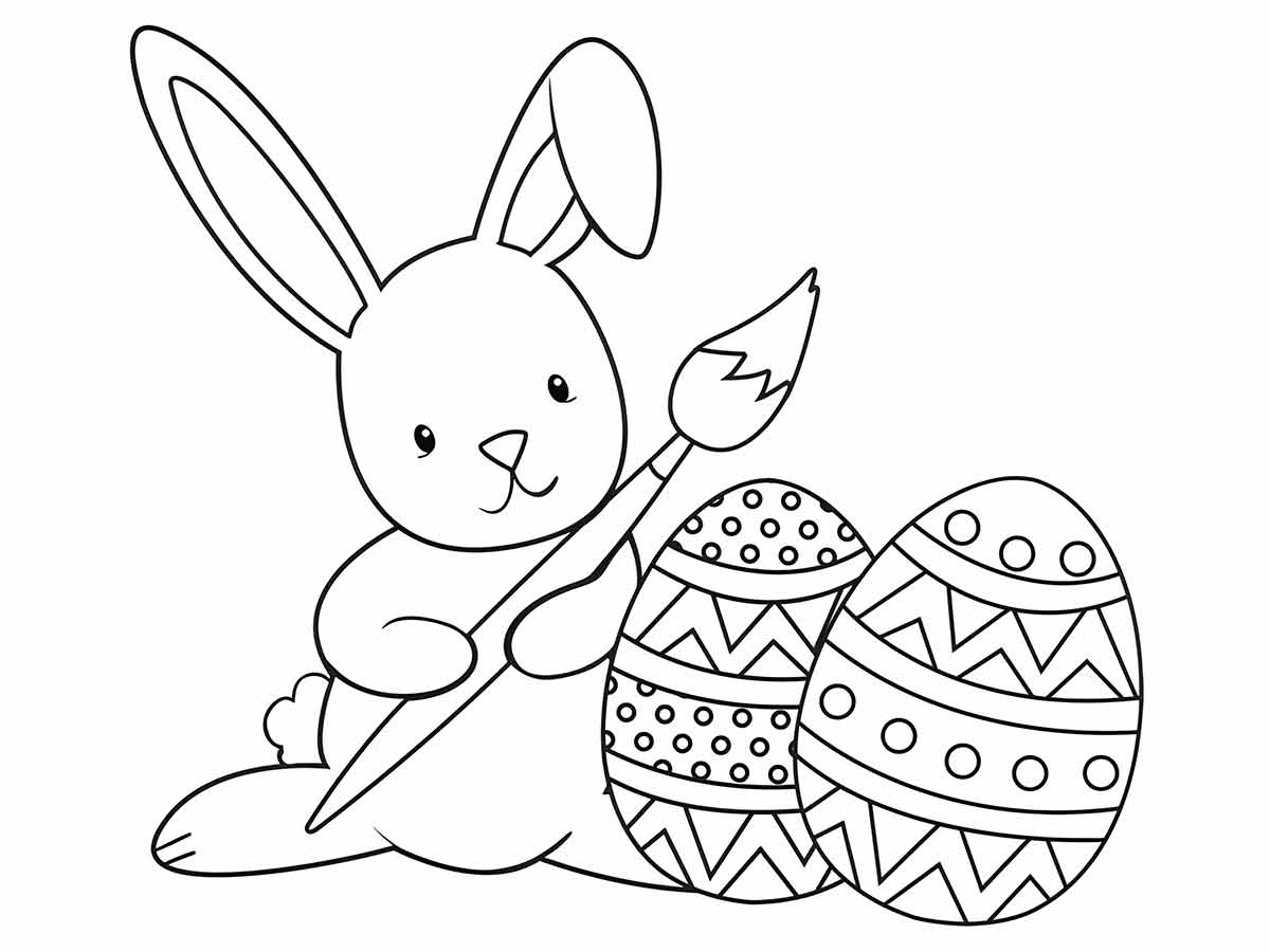 Coloring page of a bunny holding a paintbrush and sitting next to two decorated Easter eggs.